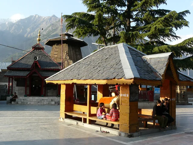 The courtyard of the Chaurasi temple complex with a wooden shelter and mountains behind