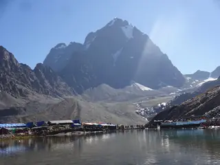 Manimahesh Lake below a steep peak with tents along its shore