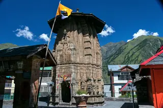 The stone tower of the Narasimha temple at Bharmour with a green mountain behind it under a blue sky