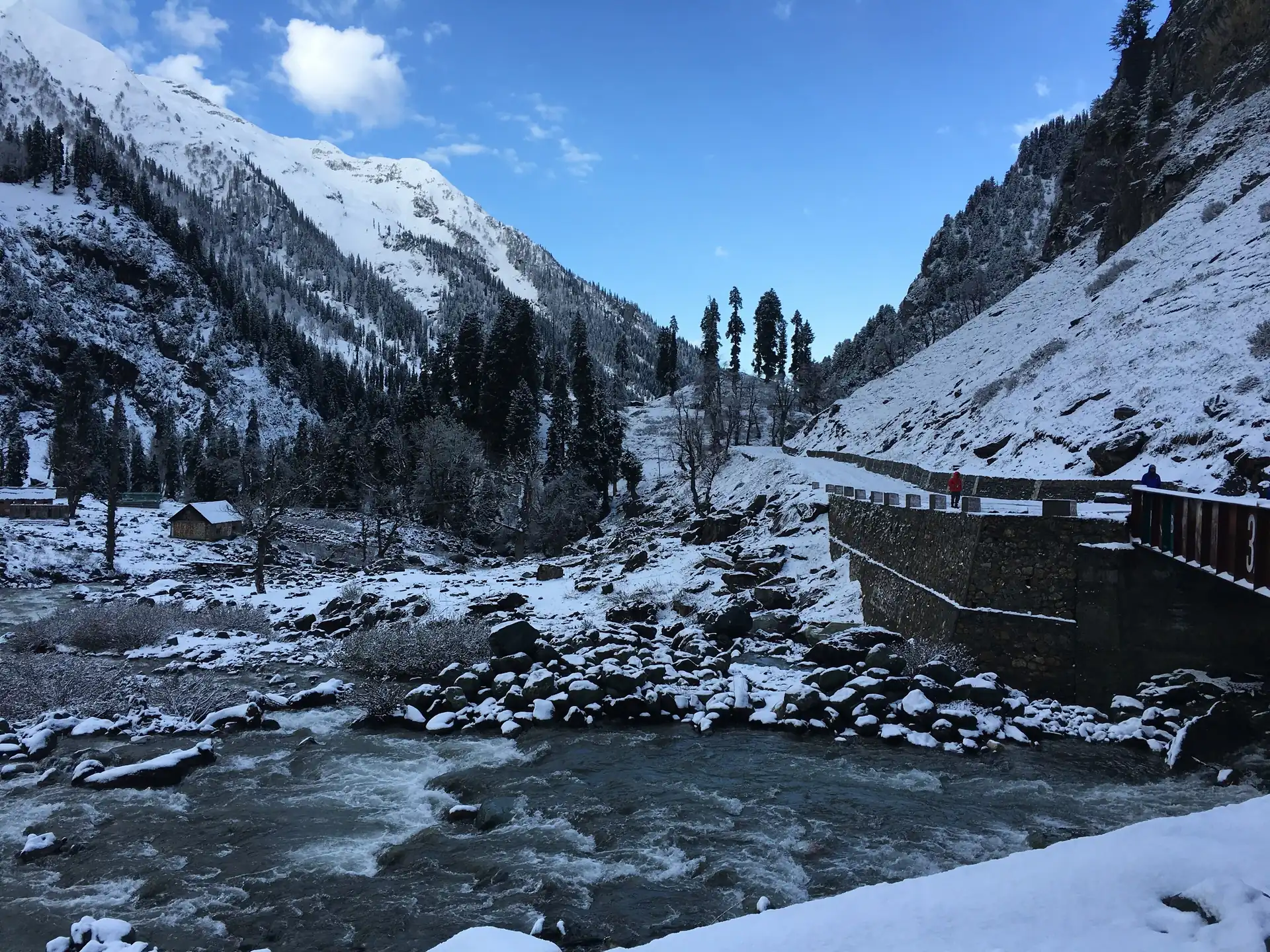 A fast stream below snowy slopes and a stone viewing platform at Chandanwari after fresh snowfall