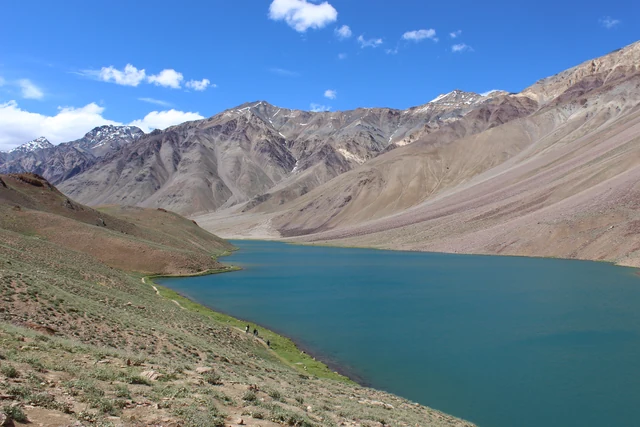 Chandratal, a curved blue lake below bare brown and grey scree slopes in Lahaul, under a blue sky