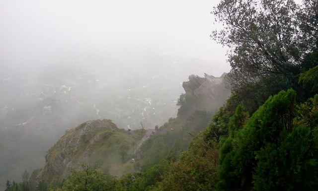 Weathered grey rock crags topped with scrub above a deep valley under a pale cloudy sky