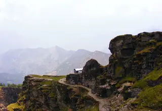A path winding along a rocky ridge on the Chandrashila trek with layered mountain ranges in a haze behind