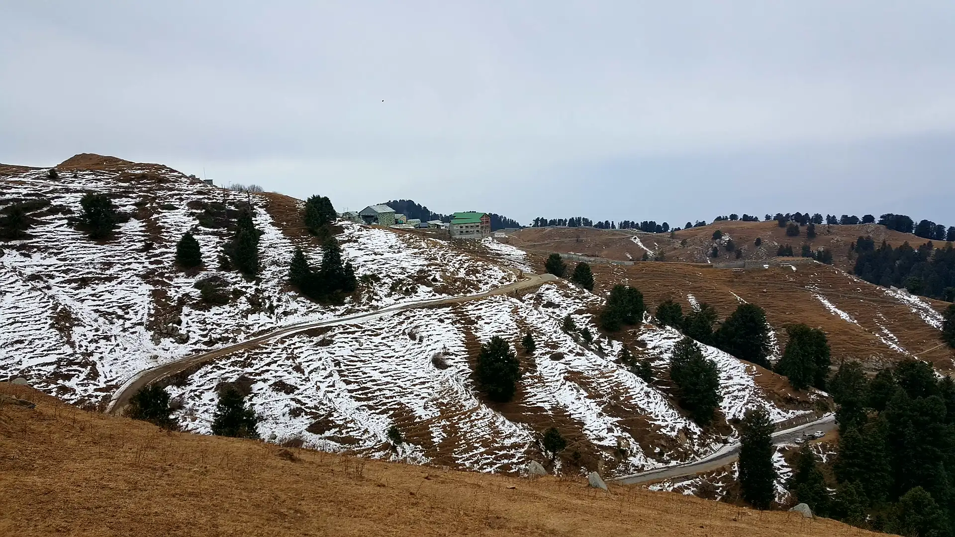 A snow-flecked ridge near Dainkund with a narrow road winding across the slope