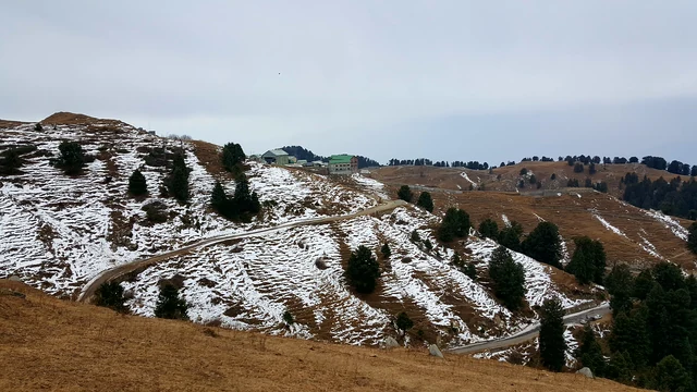 A snow-flecked ridge near Dainkund with a narrow road winding across the slope