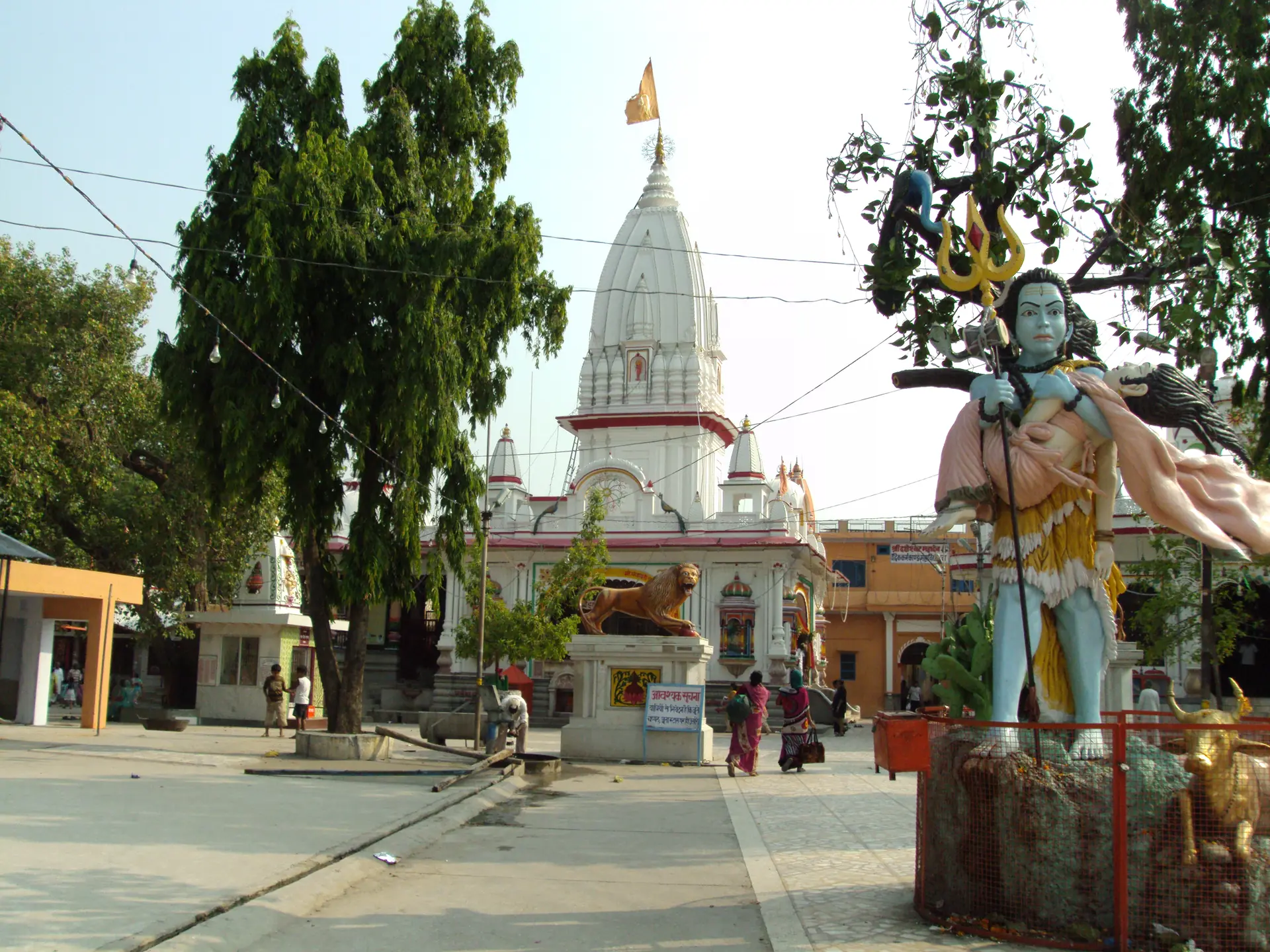 The white spire of the Daksheswara Mahadev Temple at Kankhal rising behind a large painted statue of Shiva and trees