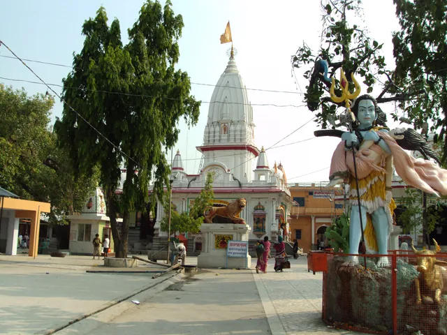 The white spire of the Daksheswara Mahadev Temple at Kankhal rising behind a large painted statue of Shiva and trees