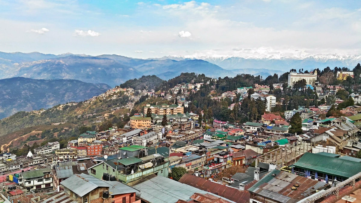 Roofs and hotels of Darjeeling spreading down a steep ridge under distant blue mountain ranges and soft cloud