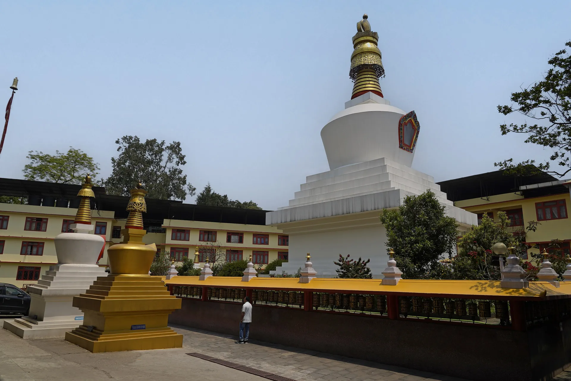 The white Do-drul Chorten with its gold spire and thirteen rings, a small gold chorten beside it and monastery buildings behind