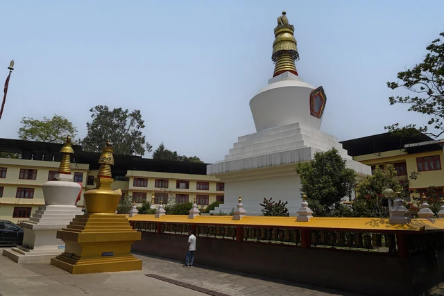 The white Do-drul Chorten with its gold spire and thirteen rings, a small gold chorten beside it and monastery buildings behind