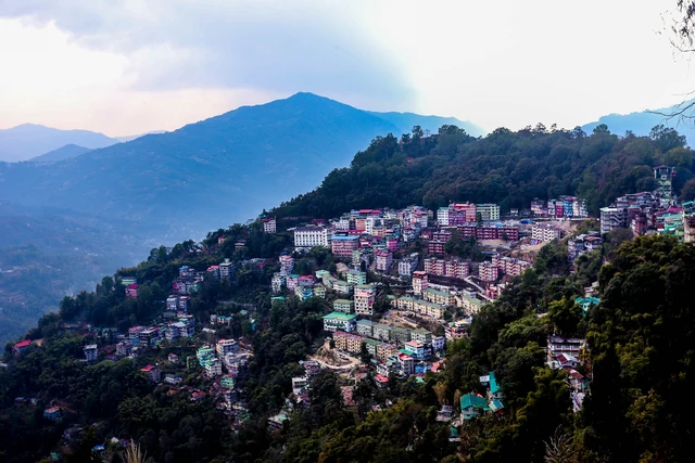 Houses and hotels of Gangtok spread along a ridge with blue ranges behind and low cloud lit by the sun