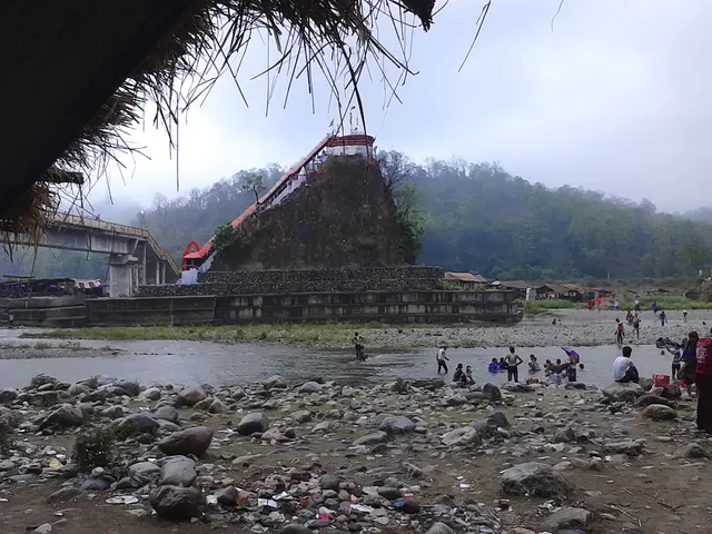The red-roofed Garjiya Devi temple on a wooded rock in the Kosi river, with people on the stony riverbed below
