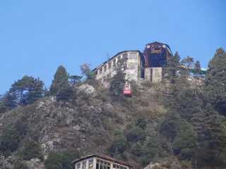 A red cable car arriving at the station on the rocky summit of Gun Hill above Mussoorie, with a building beside it