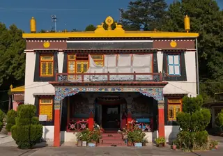 The front of the Shedup Choepelling temple in Happy Valley, a white building with a yellow roof ornament, painted red pillars and a decorated porch