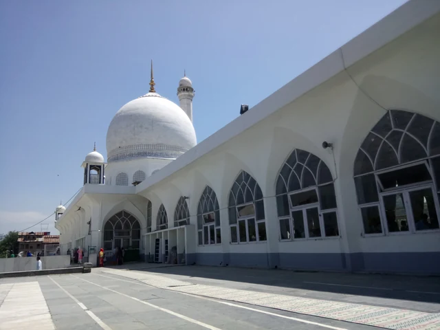 The white dome and arched cloister of the Hazratbal shrine beside an empty paved road under a blue sky