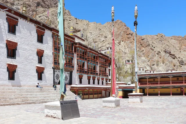 A whitewashed courtyard at Hemis Monastery with red-framed windows and tall flagpoles under a blue sky