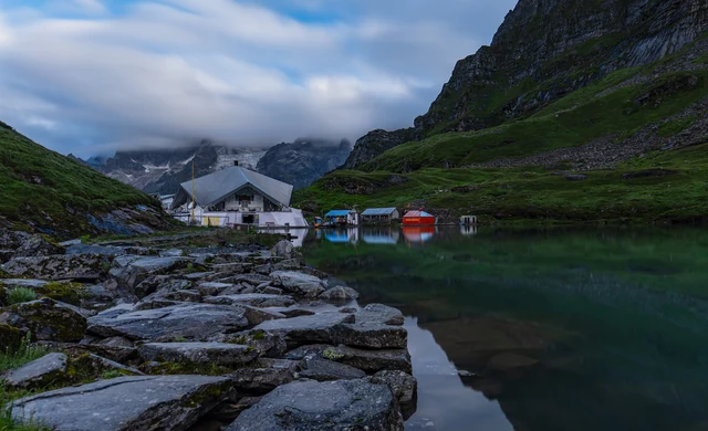 The white gurdwara of Hemkund Sahib beside its glacial lake, with rocky shore in front and mountains and cloud behind