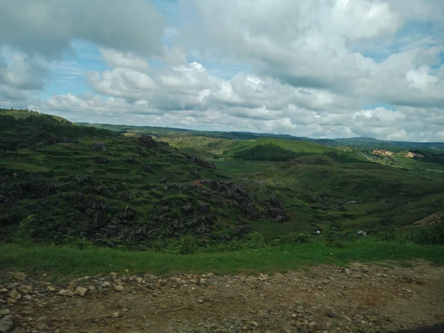 Rolling green hills of the Khasi plateau under a sky of broken cloud, seen from a roadside near Cherrapunji