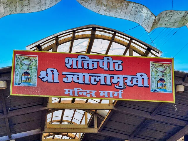 A red sign reading Shaktipeeth Shri Jwalamukhi Mandir Marg above a covered approach to the temple