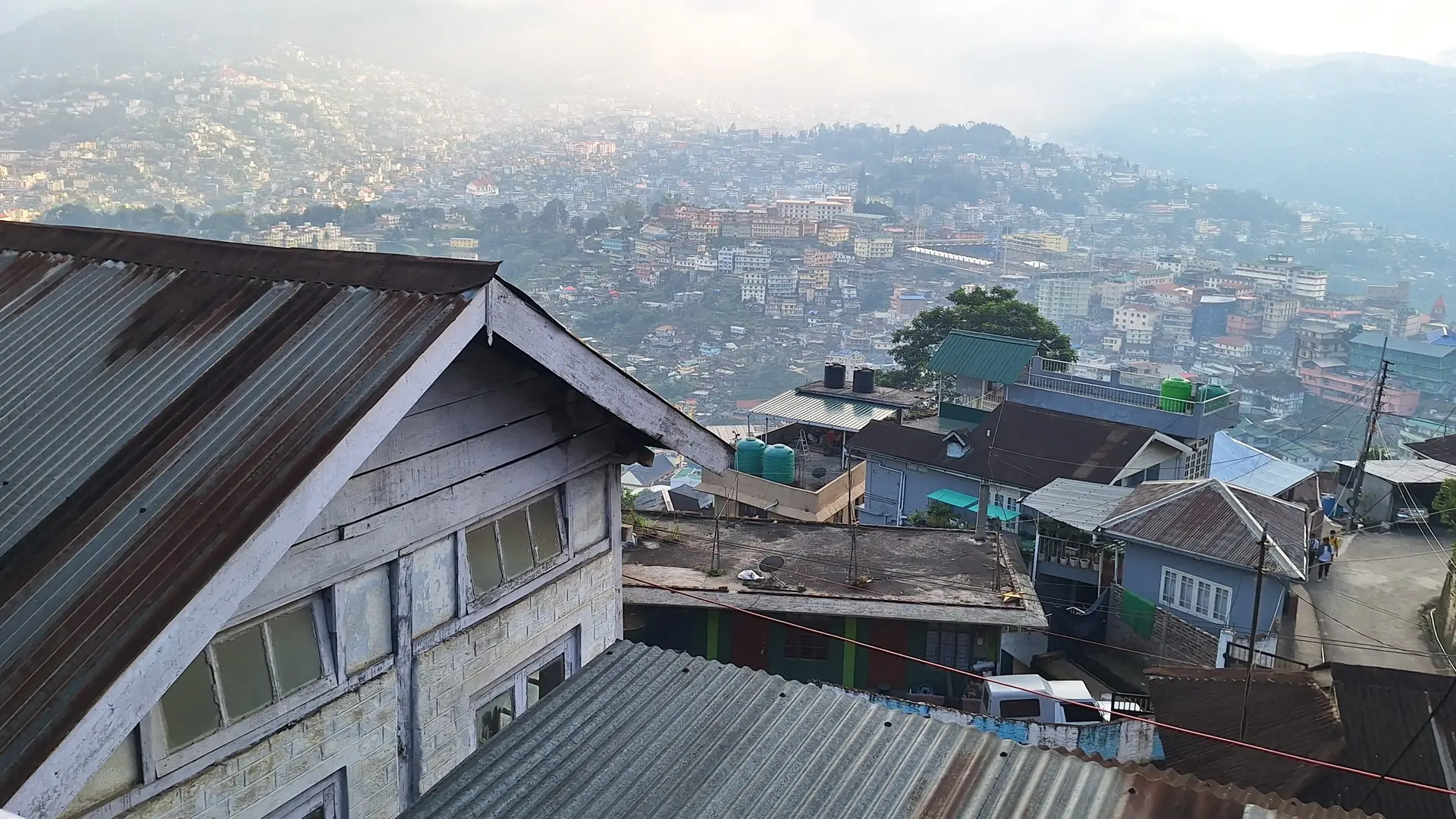 Kohima's houses spread over green ridges in the haze, seen across rooftops from Bara Basti