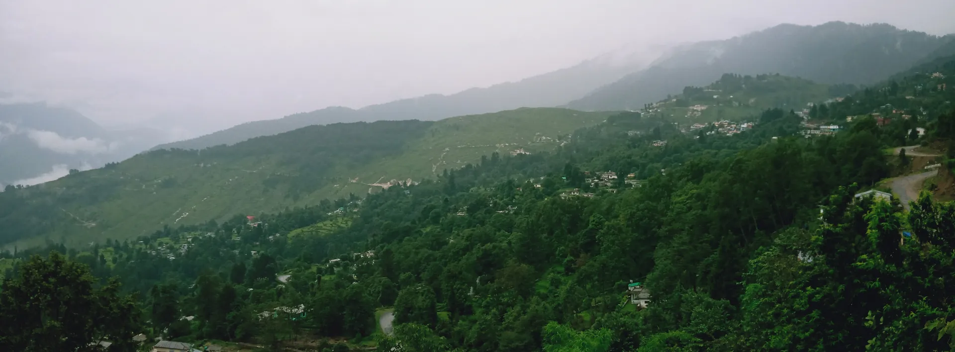 A wide view of green terraced hills and the scattered houses of Munsiyari under a hazy sky