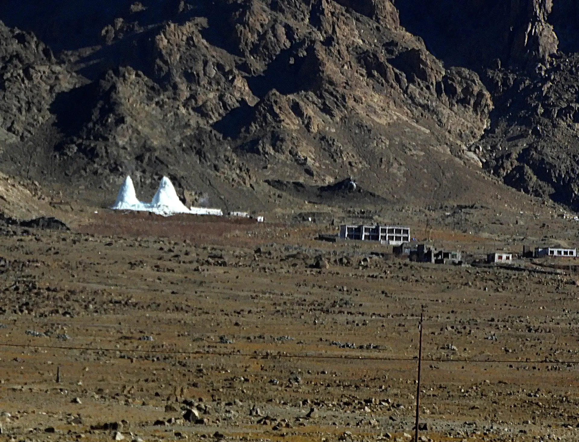 Two white ice stupas on the brown valley floor near Phyang in Ladakh, bare mountains behind