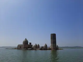 The Bathu temples standing on an island in the water of the Pong reservoir, with a tall stone pillar beside them
