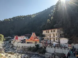 The red-spired Kainchi Dham temple and ashram buildings beside a stony stream in a forested valley in the early morning