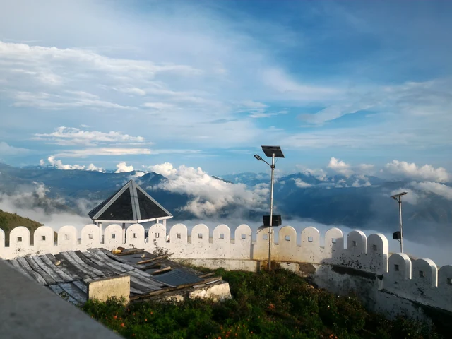 A crenellated white wall and a small shelter on the hilltop at Kali Tibba, with layered hills and cloud beyond