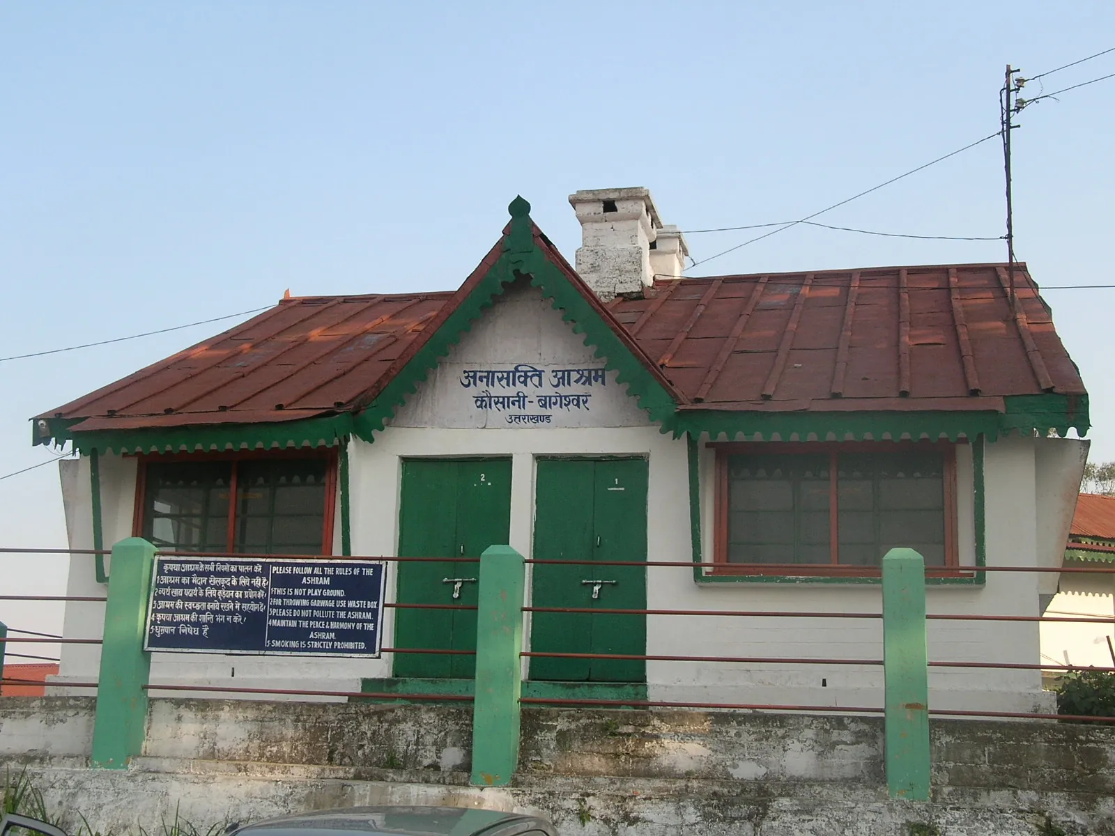 A small white and green wooden bungalow with a red tin roof at the Anasakti Ashram in Kausani