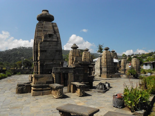 A cluster of ancient grey stone temple towers on a paved terrace under a blue sky with a few white clouds at Baijnath