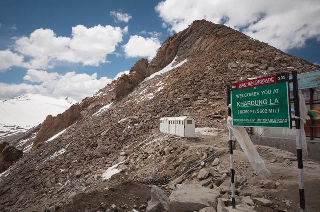 The green summit sign at Khardung La in Ladakh, with the bare brown ridge and snow behind it