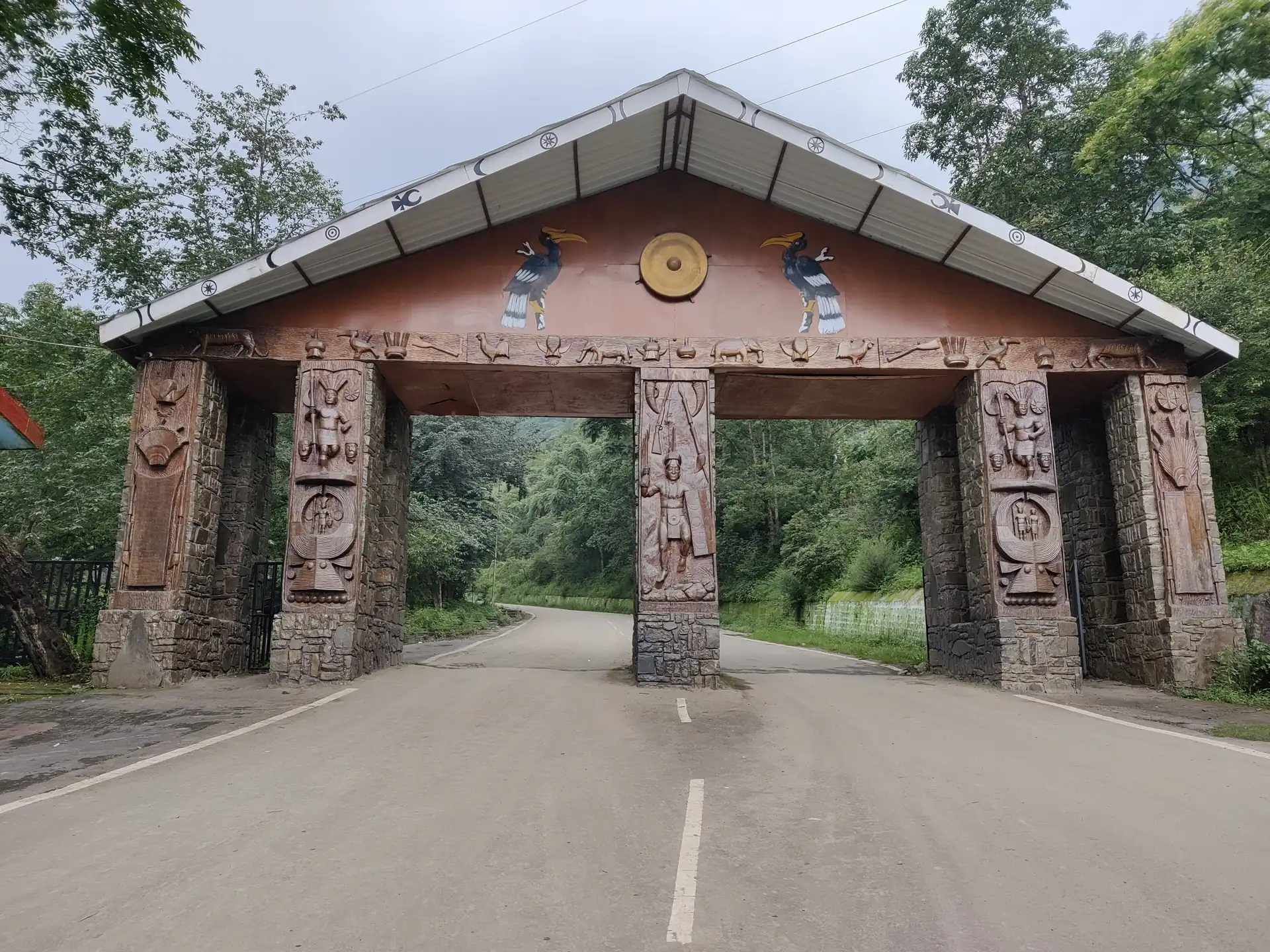 A carved wooden gateway with Naga motifs and a sloping roof over the road into the Kisama Heritage Village