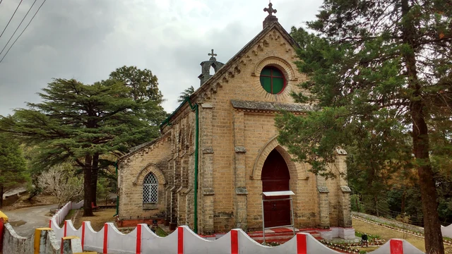 The stone Gothic front of St Mary's Church with a round window, a red door and tall deodars beside it
