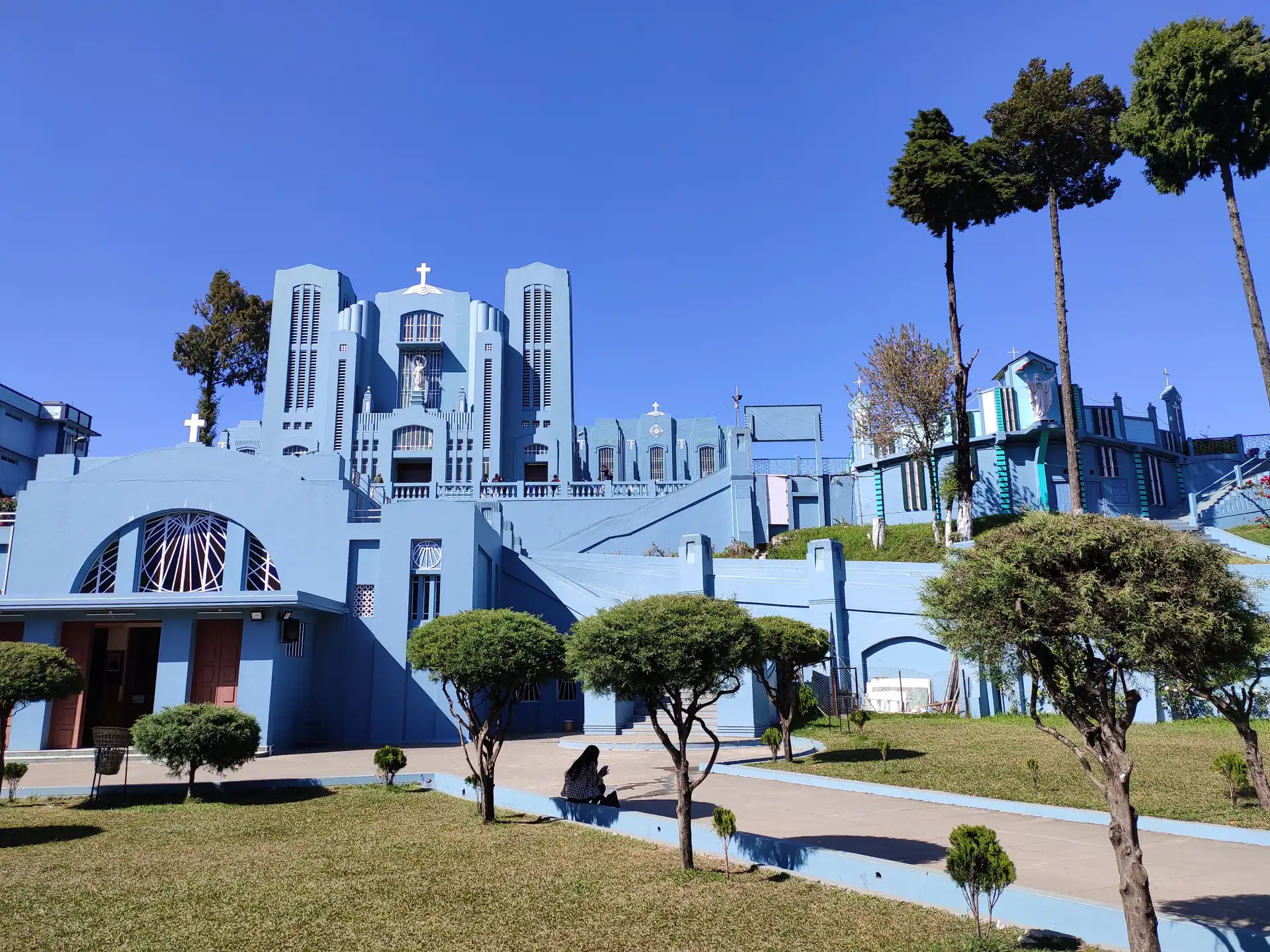 The blue and white Art Deco front of the cathedral seen over a lawn with clipped round trees under a clear blue sky