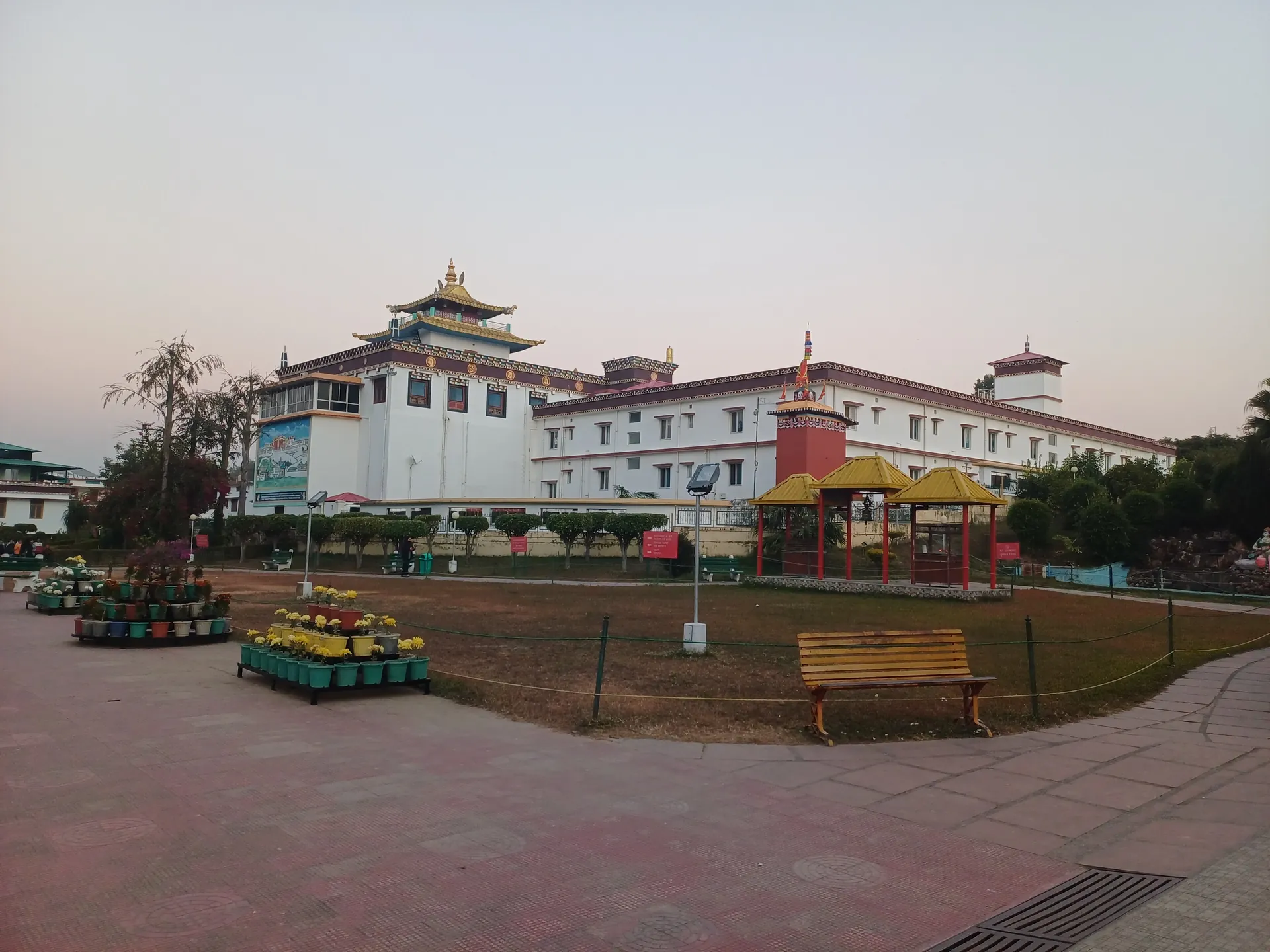 The white and red Mindrolling monastery building with a Tibetan-style roof across a paved garden at dusk