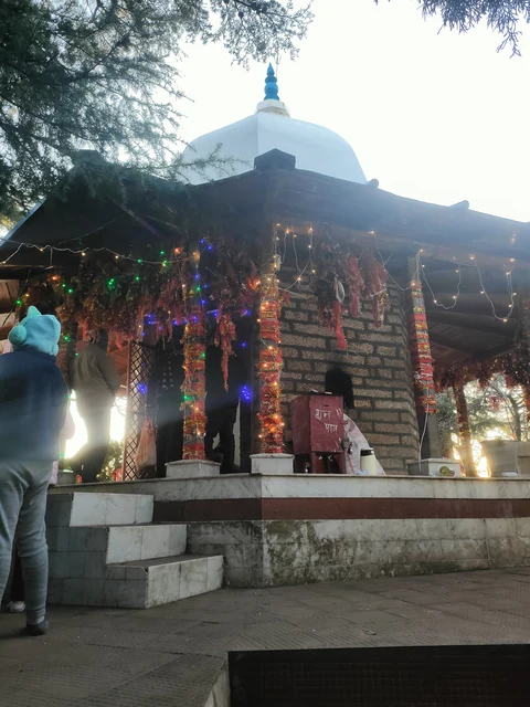 A small domed shrine lit with garlands and lamps, with worshippers on its steps