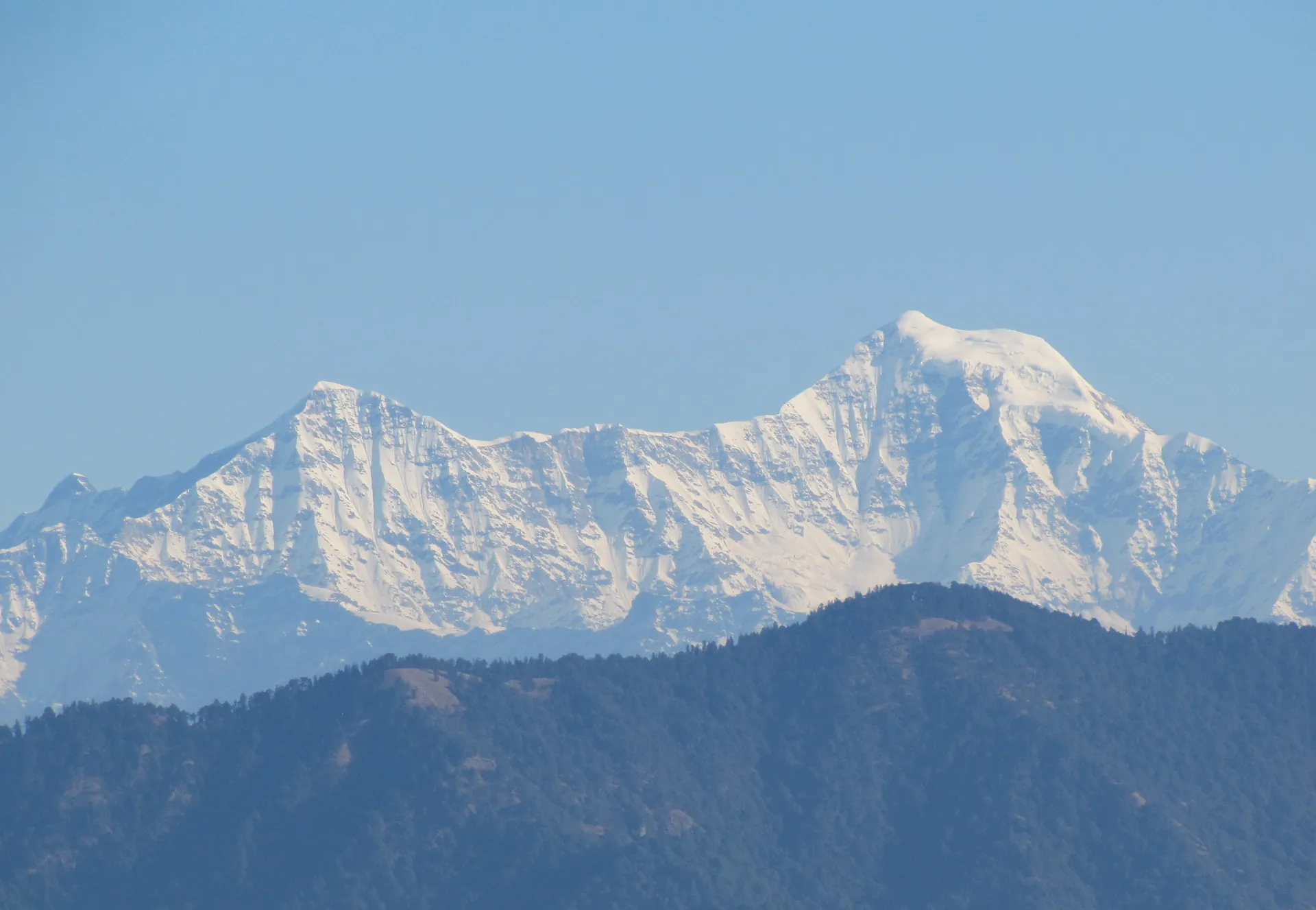 A snow-covered summit of the Bandarpunch range rising over lower blue ridges, seen from Lal Tibba at Landour
