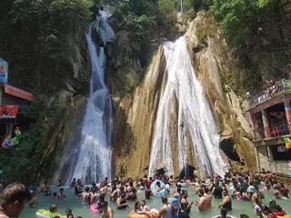 Kempty Falls in May 2024, two white streams dropping down a rock face into a plunge pool crowded with visitors