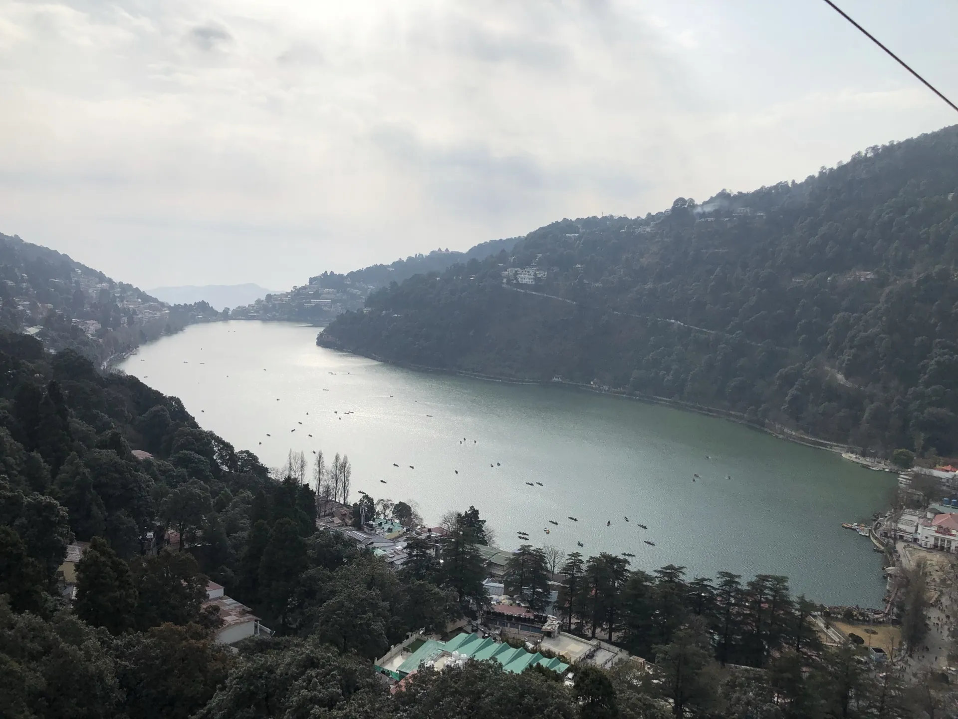 The crescent of Nainital Lake seen from above, with boats on the water and forested slopes on both sides