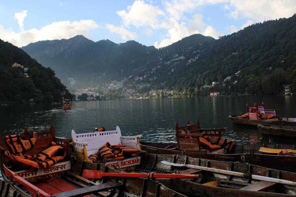 Rows of boats with red cushioned seats moored on Nainital Lake, with forested hills across the water