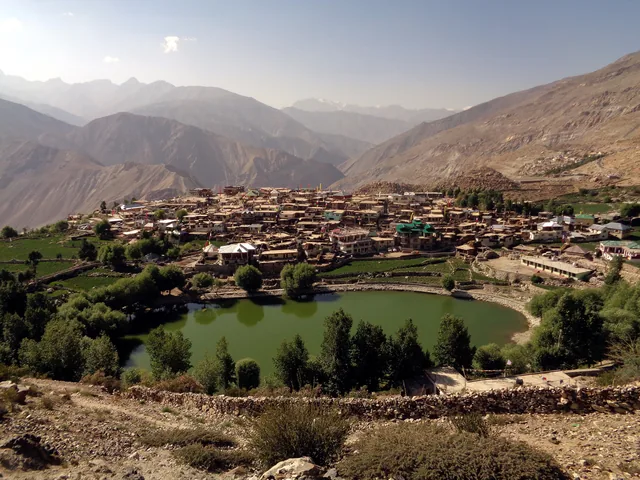 Nako village and its small green lake on a bare mountain slope in Kinnaur, with ridges behind