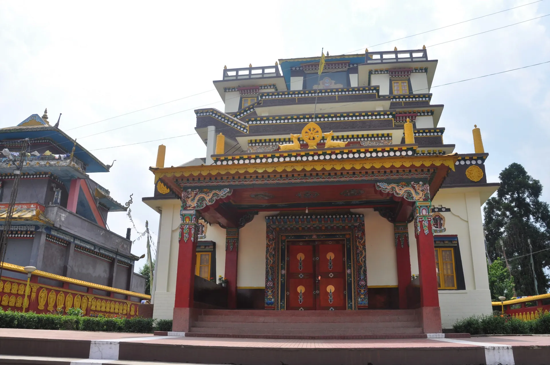 The painted front of Namchi Monastery with a red door, tiered golden roofs and white walls under a pale sky