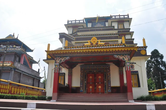 The painted front of Namchi Monastery with a red door, tiered golden roofs and white walls under a pale sky