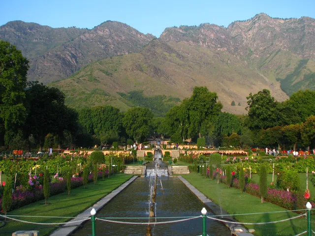 A central water channel with fountains and flower beds climbing the terraces of Nishat Bagh below dry mountains