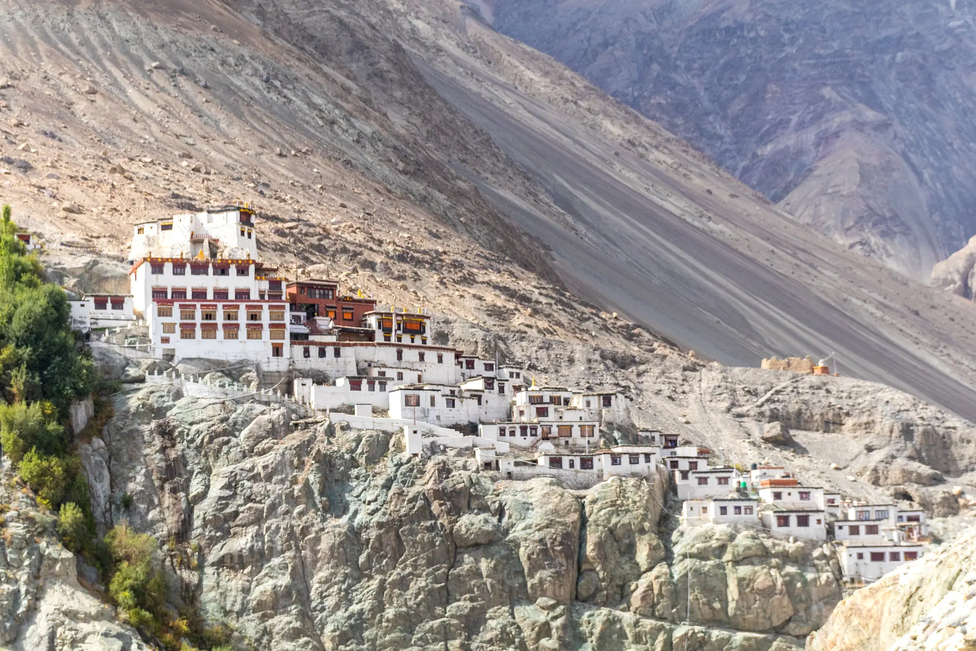 The white buildings of Diskit Monastery climbing a steep rocky slope above the Nubra valley, with bare grey mountains behind