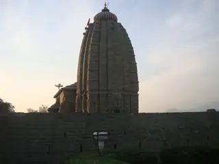 The stone tower of Baijnath Temple at dusk above the compound wall
