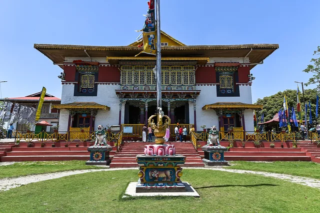 The white and red front of Pemayangtse Monastery with a flagpole and a green lawn under a clear sky