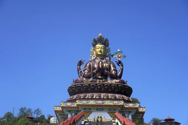 The gilded Chenrezig statue seated on a tiered lotus plinth against a deep blue sky with red stair rails running up to it