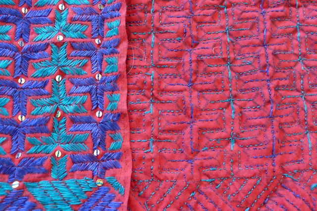 A phulkari shawl from Punjab folded to show both faces: blue and turquoise silk on the left, the reverse with small stitches on the right